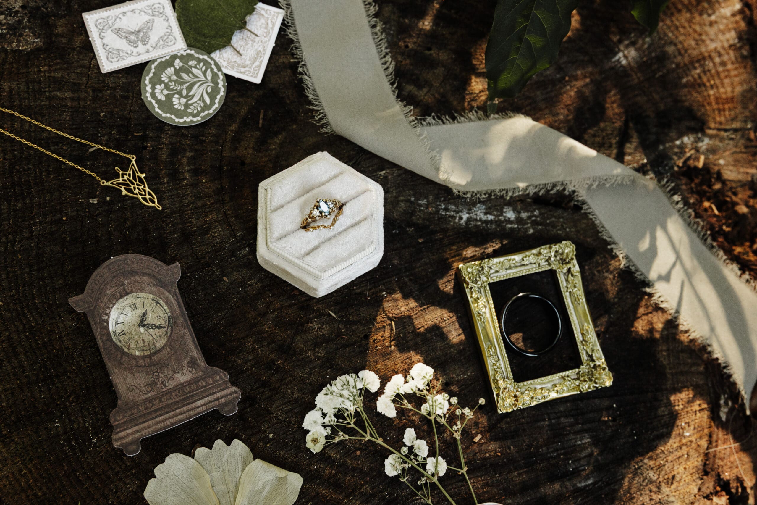 Woodsy fairytale georgia wedding detail flat lay with vintage ring box, wedding rings, silk ribbon, floral accents, and antique-inspired elements on dark wood