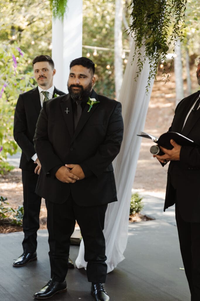Groom watching bride walk down the isle in woodsy fairytale wedding.