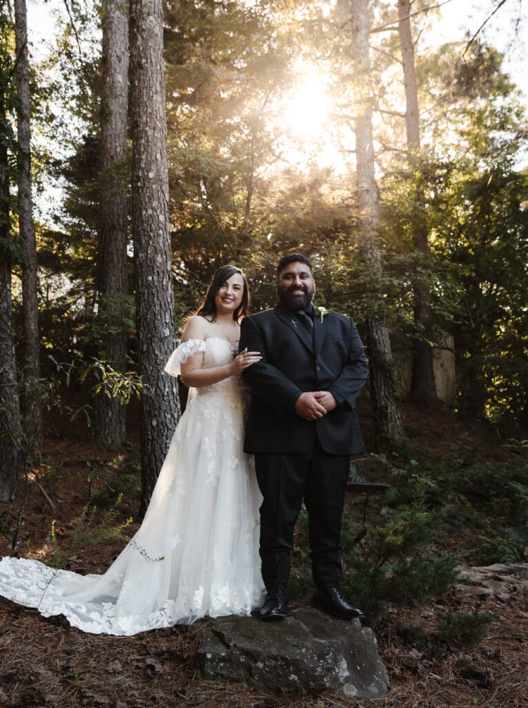 Bride and groom standing together in a Georgia forest during a woodsy fairytale wedding, framed by tall trees and golden sunlight