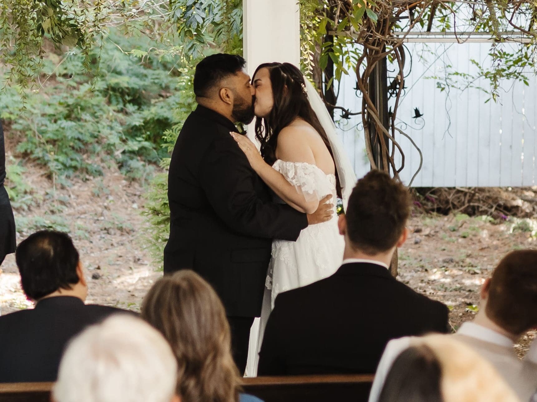 Emotional ceremony moment as bride and groom stand together under a greenery-covered pavilion