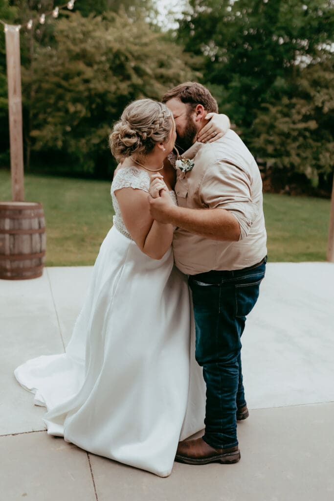 Bride and groom sharing an intimate dance and kiss during their outdoor barn wedding reception in Georgia, captured in a natural documentary photography style.
