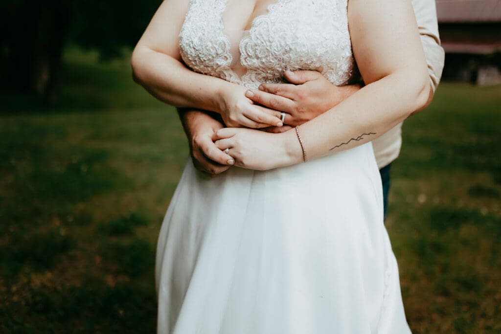 Close-up of the bride and groom embracing, hands intertwined at her waist, highlighting rings and quiet connection.