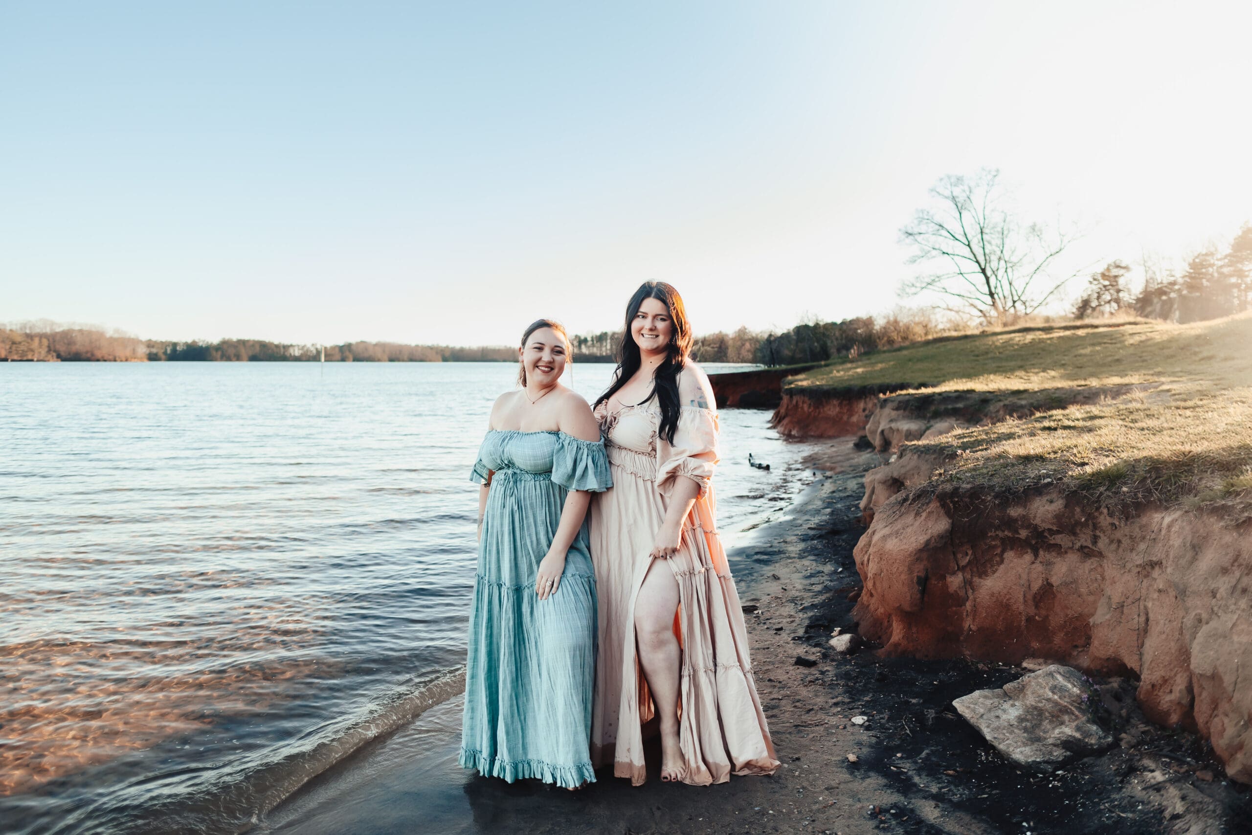Two women in dresses posing on lakeshore for a best friend photo session.