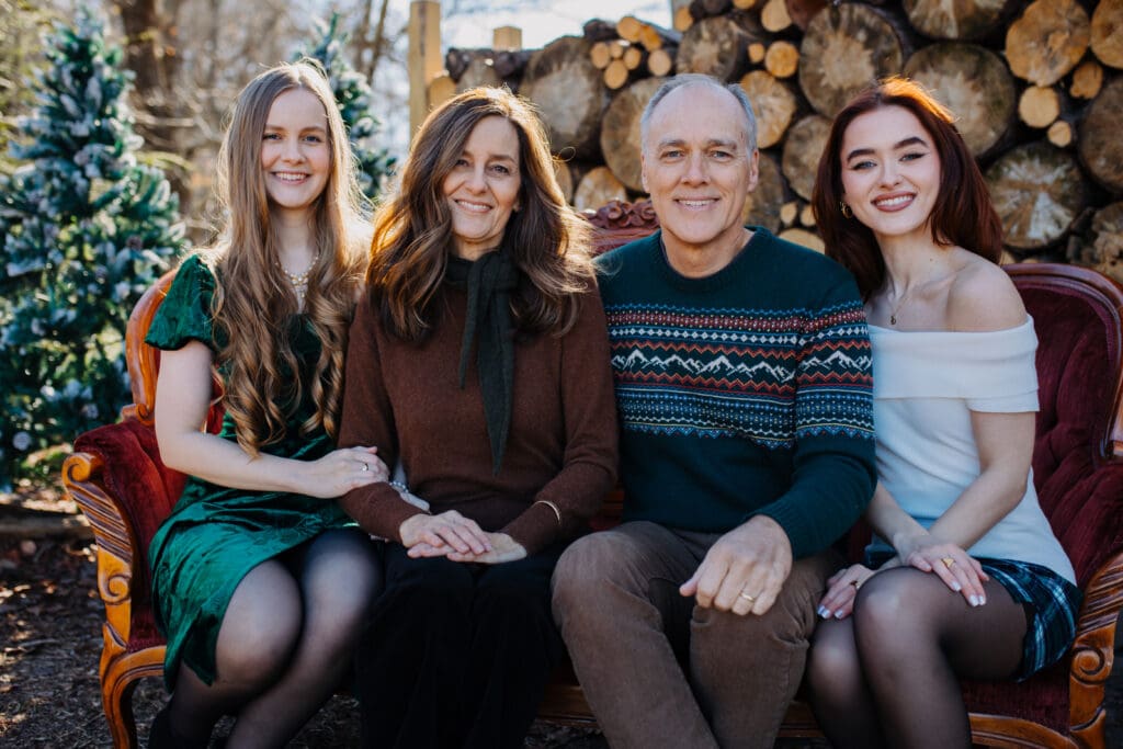 Cozy holiday family portrait by a Georgia lifestyle family photographer featuring parents and daughters seated together on a vintage couch outdoors.