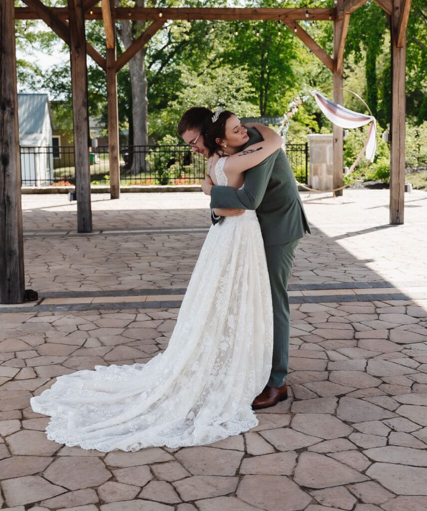 Bride and groom embrace under a wooden pavilion surrounded by greenery during their intimate wedding portraits