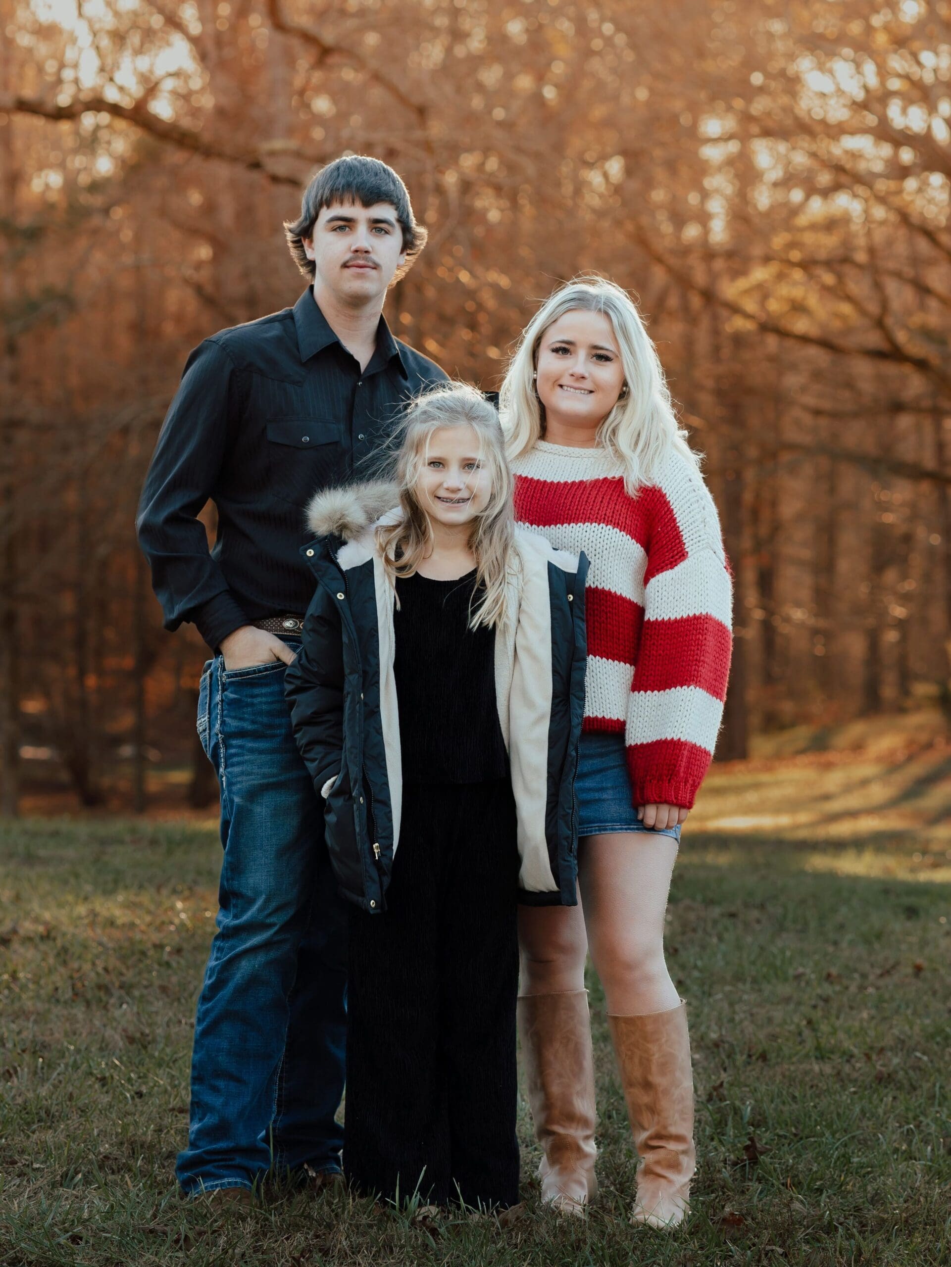 Sibling family portrait photographed by a North Georgia family photographer featuring teens and a child standing together outdoors in a wooded fall setting.
