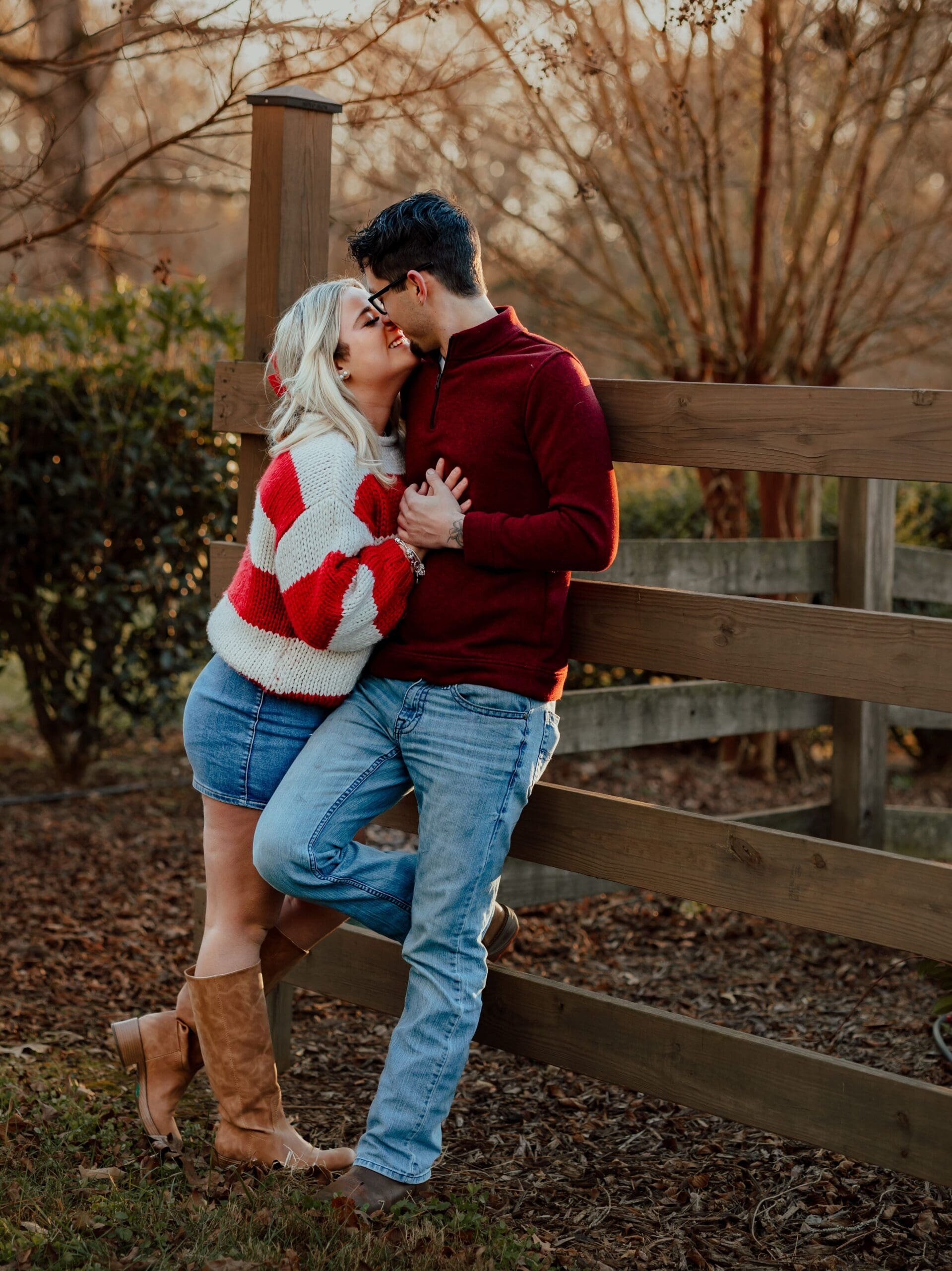 Candid young couple portrait showing a couple leaning together by a wooden fence during golden hour.