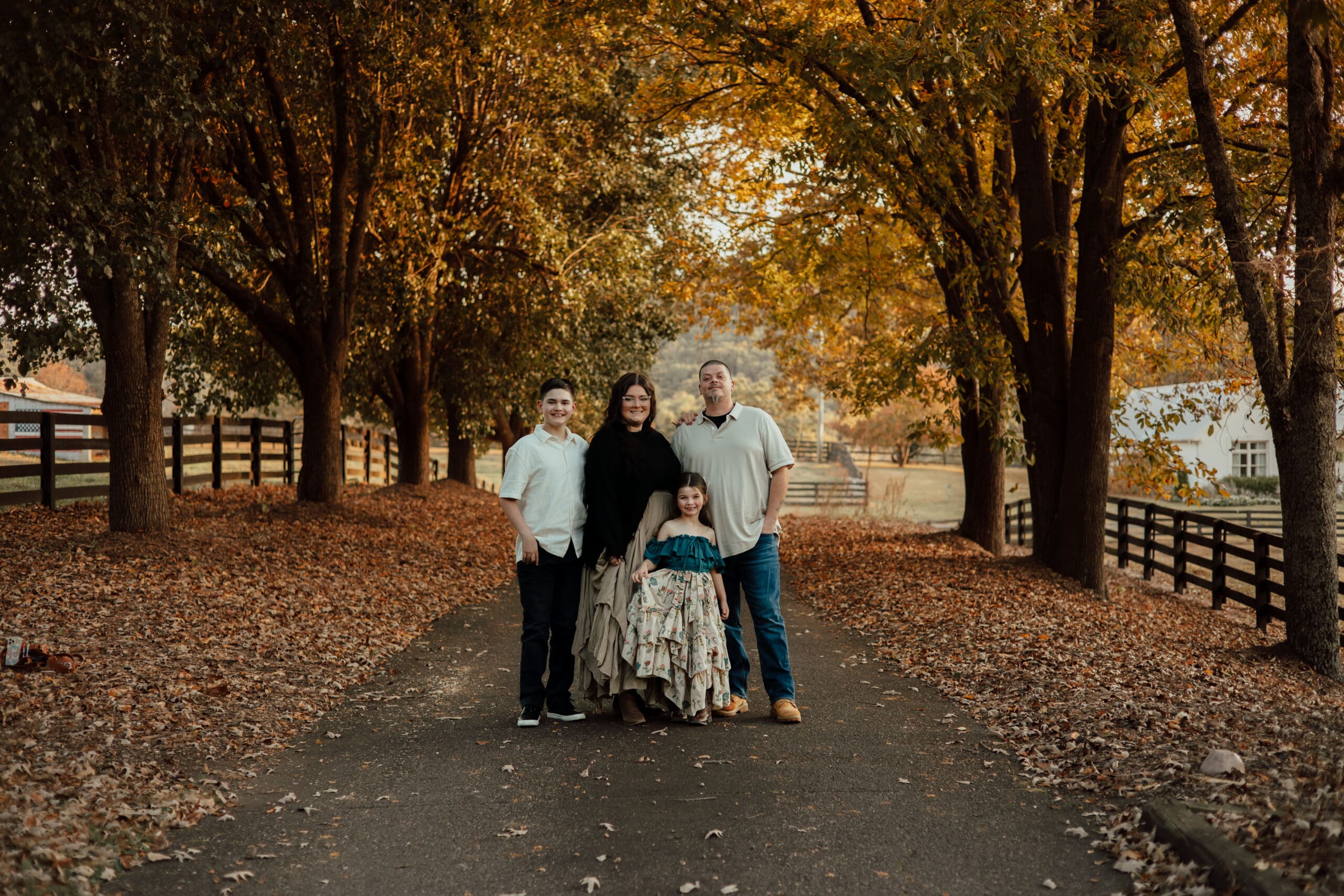 Family of four standing together on a tree-lined road during fall in North Georgia, surrounded by golden autumn leaves