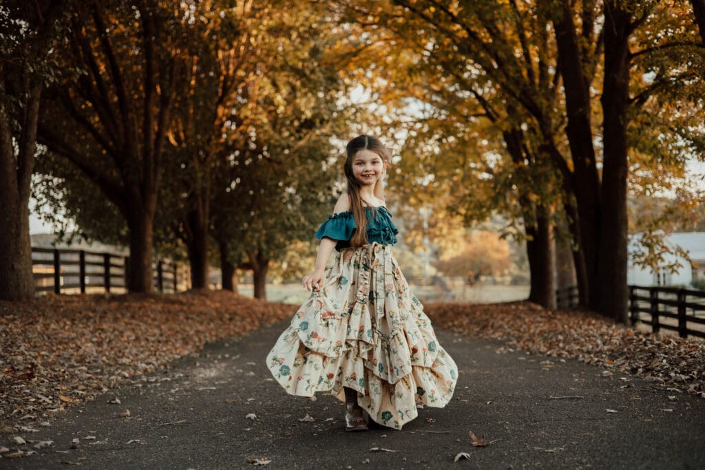 Gainesville Family Photographer, Young girl walking down a tree-lined path during a family photo session wearing a floral dress at golden hour.