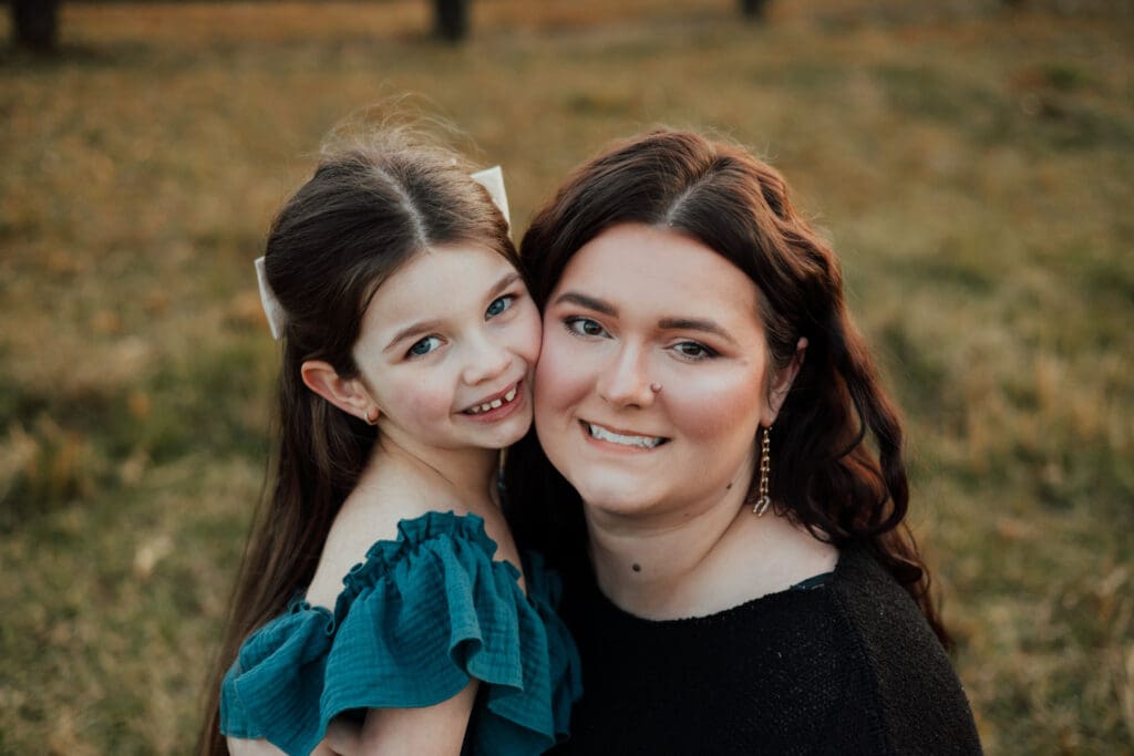 Mother and daughter smiling together during a photo session, captured in soft natural light.