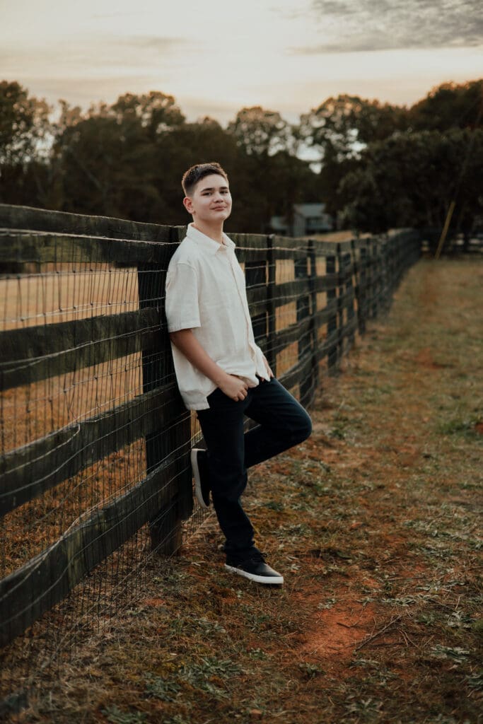Gainesville Family Photographer, teen boy leaning against a wooden fence during a family photo session at golden hour.