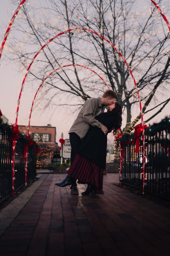 Cozy holiday engagement portrait featuring a couple wrapped in winter layers, surrounded by Christmas decor and twinkle lights