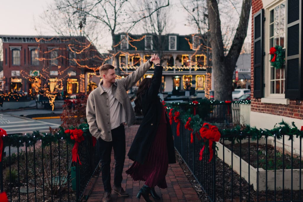 Georgia engagement photographer photographing a playful engagement twirl beneath glowing holiday lights and festive garlands