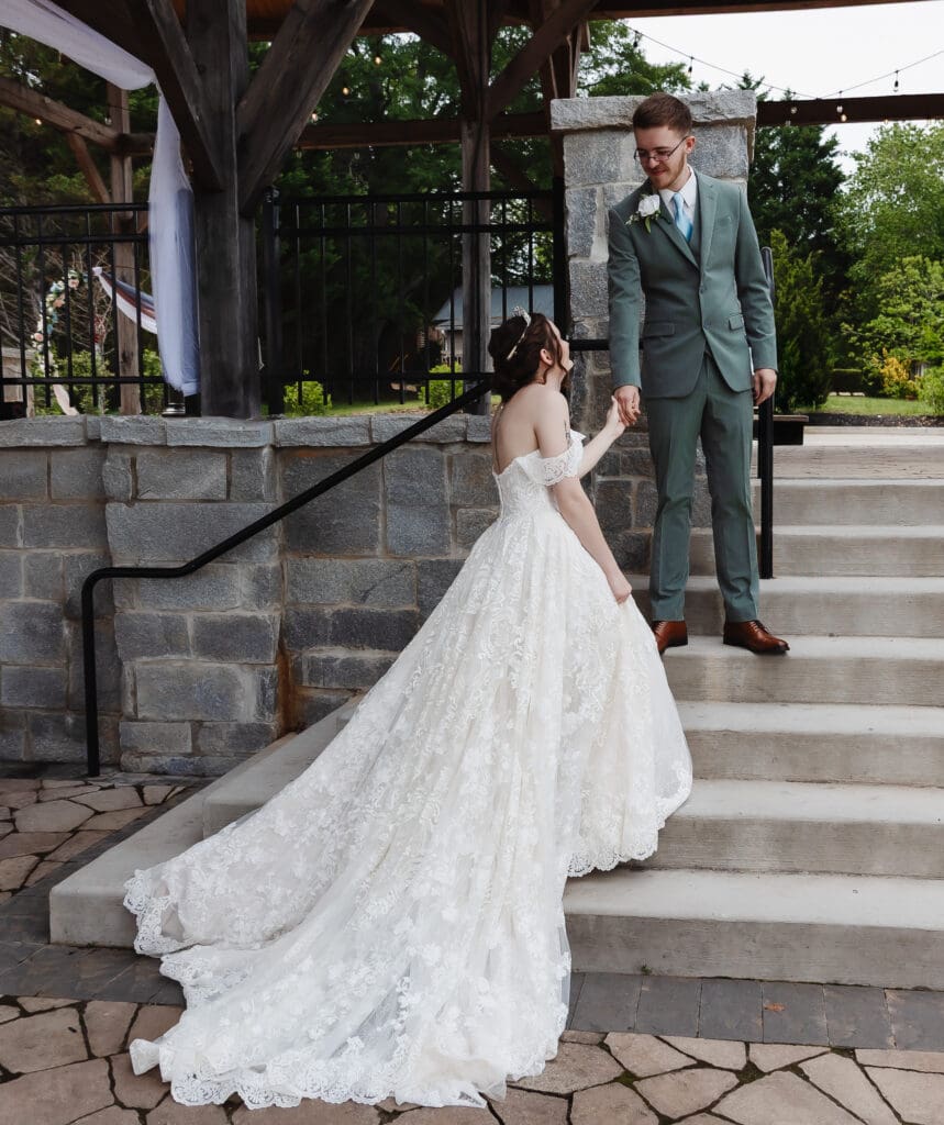 Groom gently helps his bride down stone steps after their ceremony, highlighting a quiet moment during their intimate wedding day