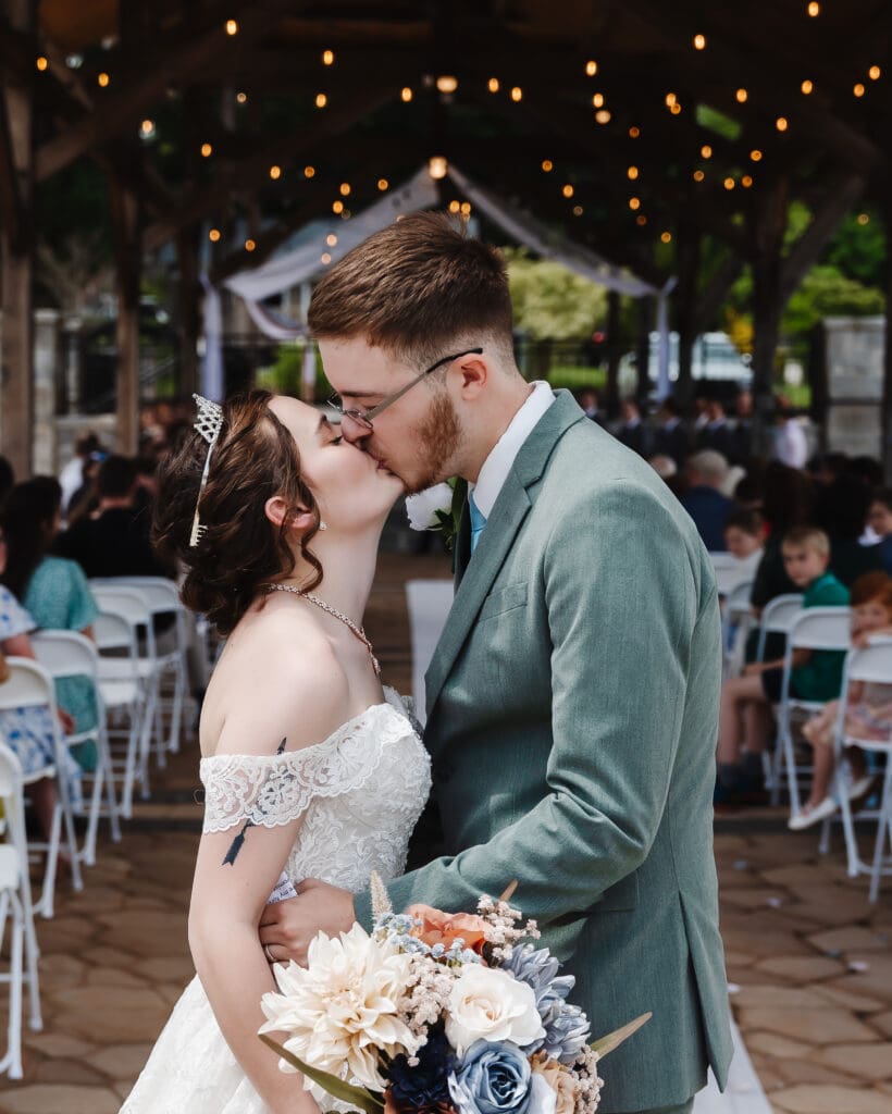 Bride and groom share their first kiss beneath a wooden arbor during an intimate outdoor wedding ceremony in Georgia