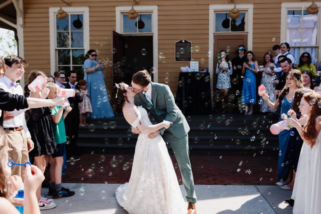Bride and groom share a joyful kiss during their intimate wedding exit as guests blow bubbles outside a historic Georgia venue