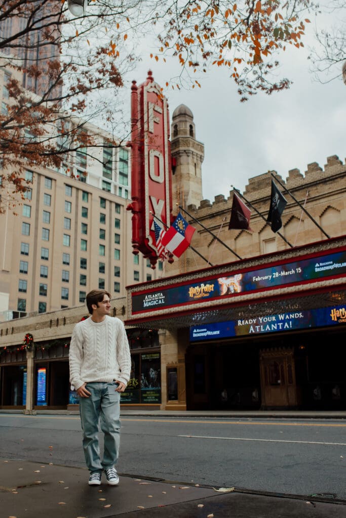High school senior standing on the sidewalk in front of the Fox Theatre sign in downtown Atlanta during senior session portraits