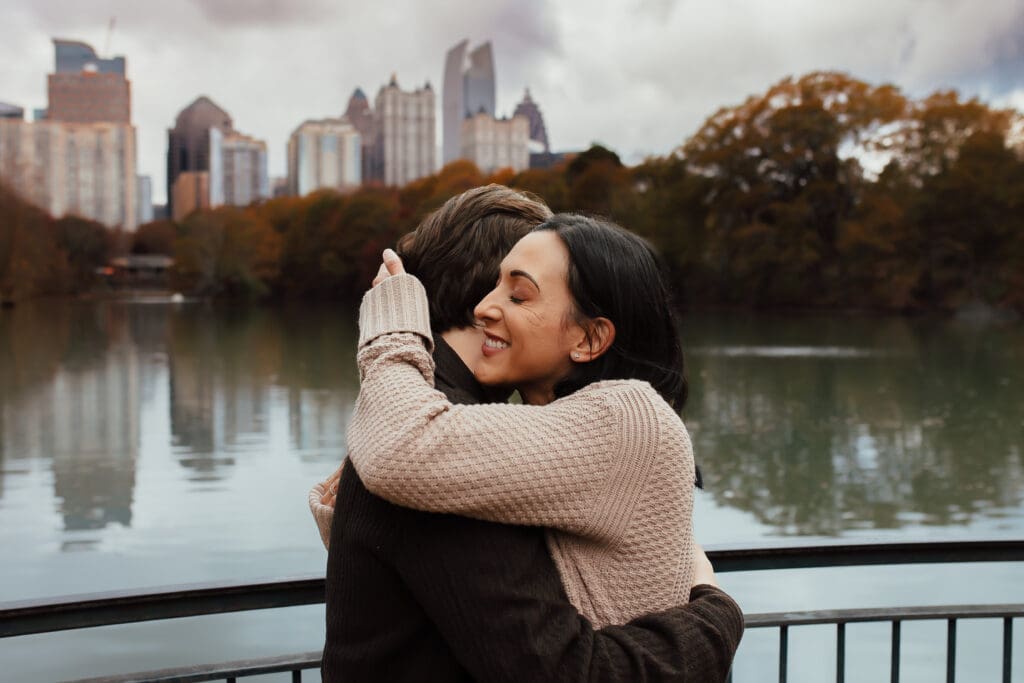 Emotional moment of a senior hugging his mother with the Atlanta skyline reflected on the water at Piedmont Park during senior session