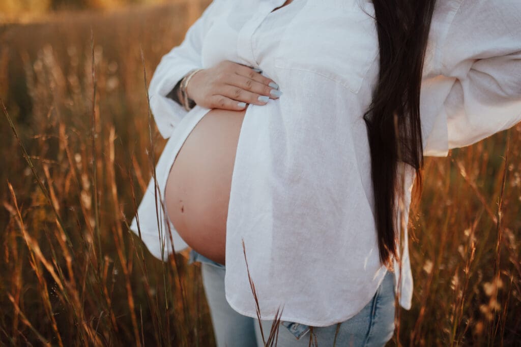 Close-up maternity detail of baby bump with soft natural light and neutral tones