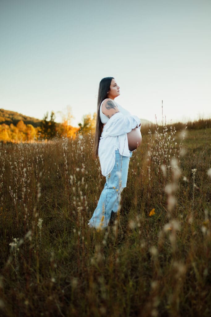 Side profile maternity portrait of an expectant mother standing in an open field with soft fall tones