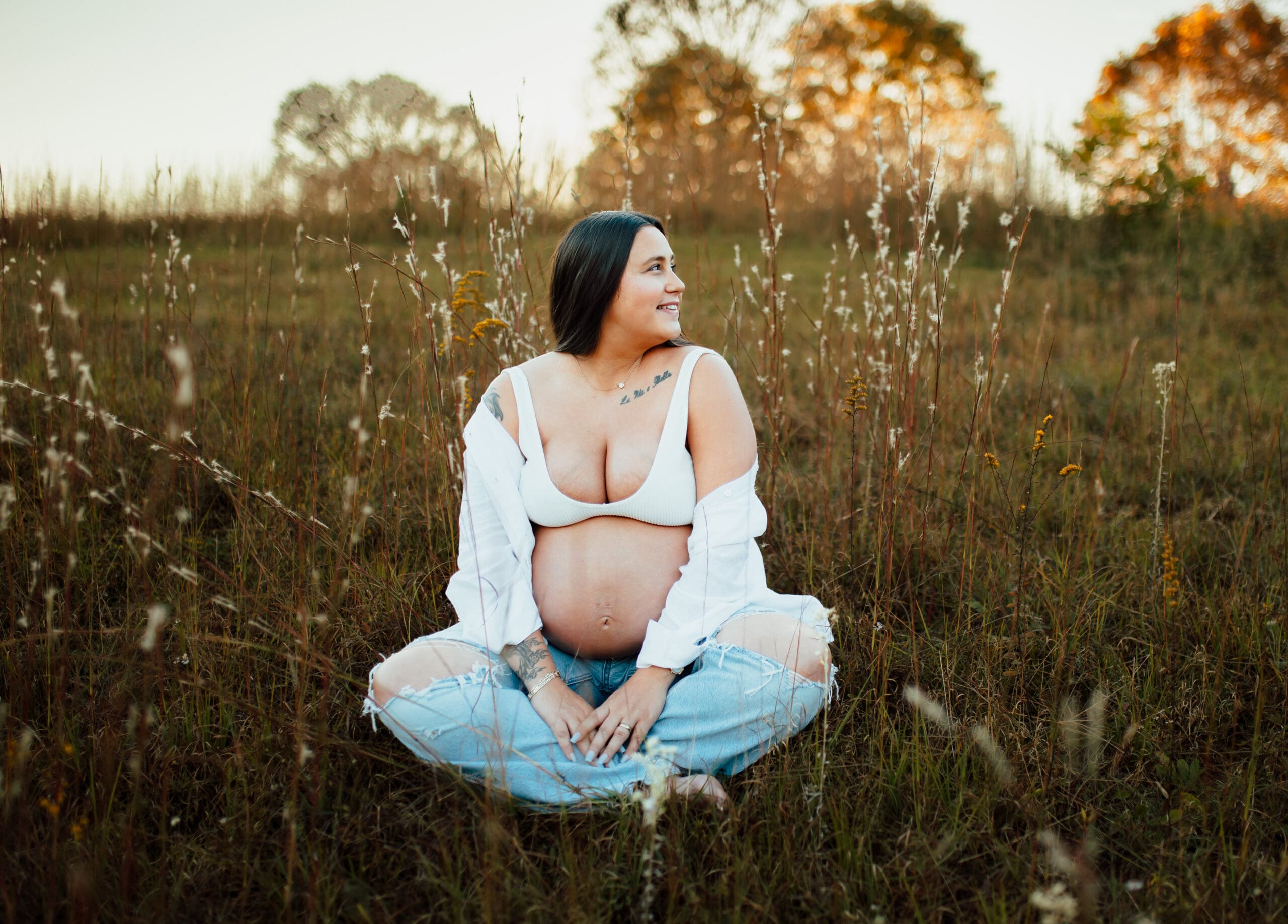 Pregnant mother gazing into the distance, wrapped in natural light and tall grass during maternity photography