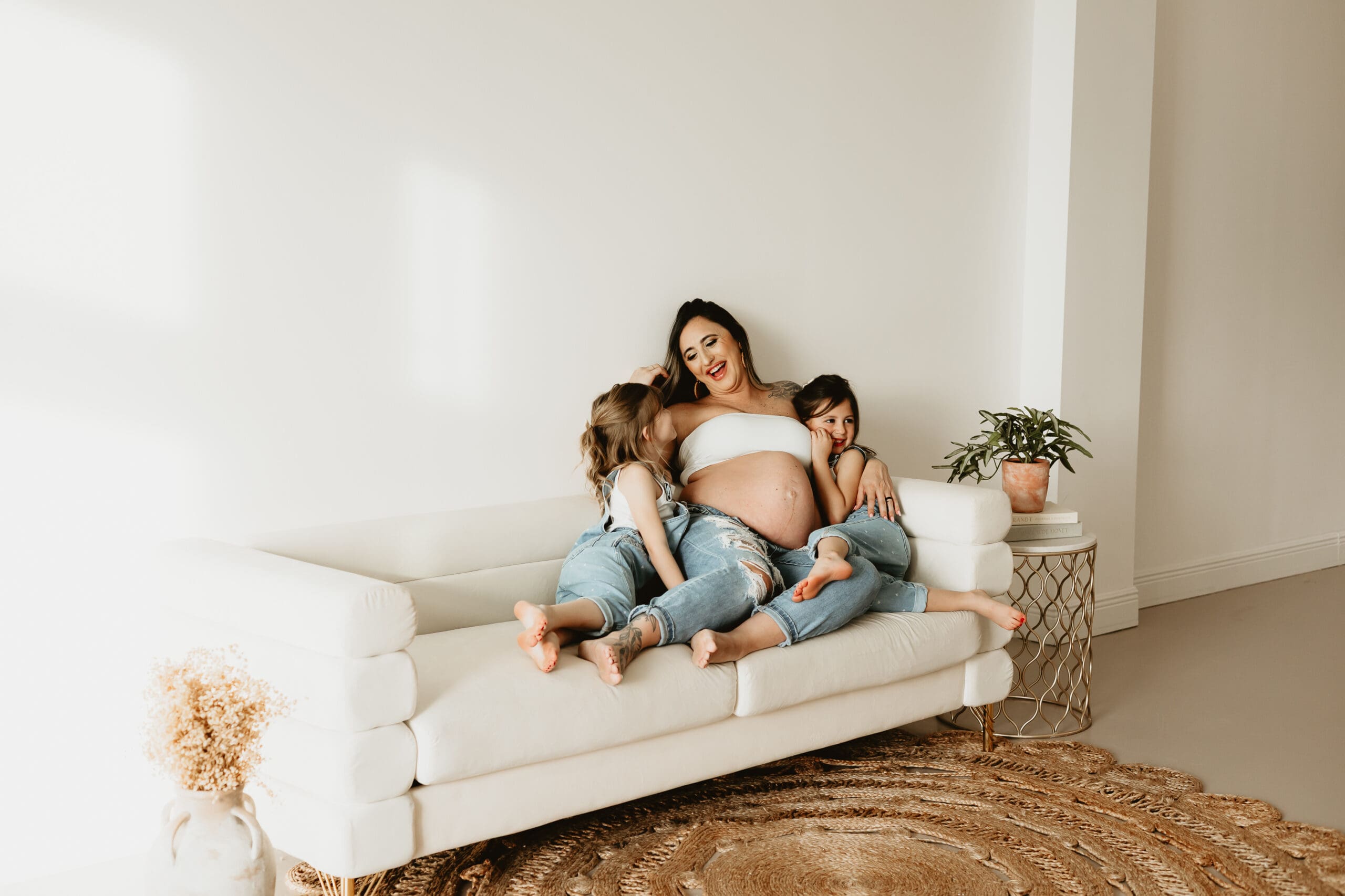 Cumming Georgia maternity photography session at Wildhaven Studio featuring a pregnant mother sitting on a white couch with her two daughters in a bright natural light studio.