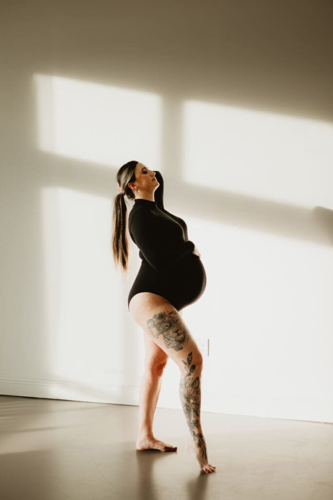 Elegant maternity portrait at Wildhaven Studio in Cumming Georgia showing a pregnant mother standing in natural window light during a motherhood photography session.