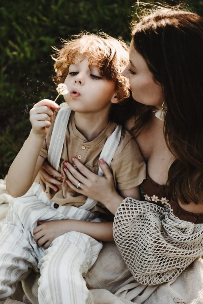 Little boy blowing a dandelion during a motherhood photography session in the fields of Cleveland Georgia.