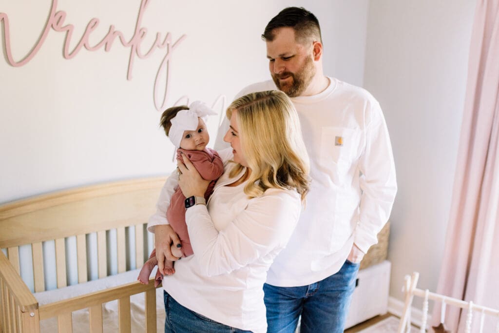Mom holding her baby girl in a nursery beside the crib during a lifestyle newborn session in Cumming, Georgia.