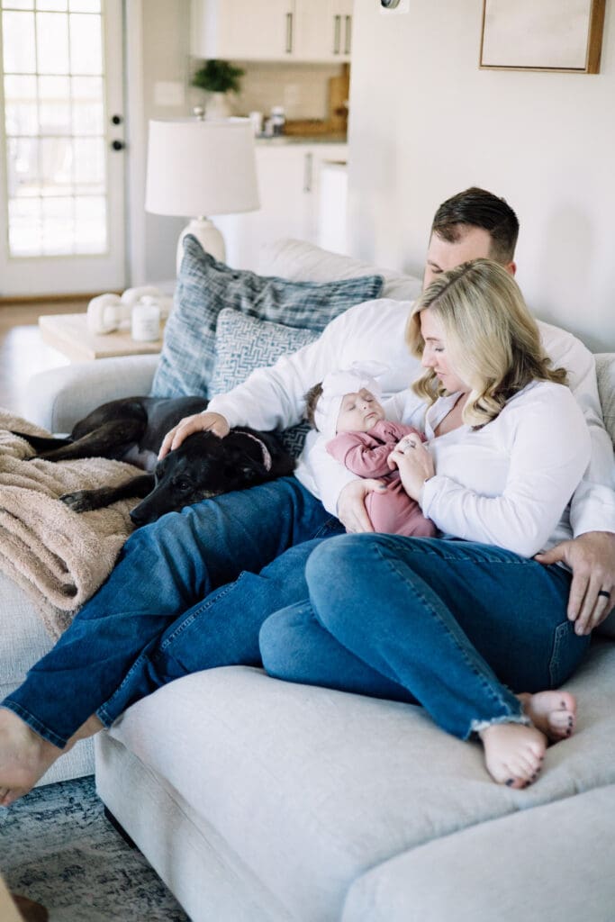 Mom and dad cuddling their baby girl on the couch with their dog during a lifestyle in-home session.