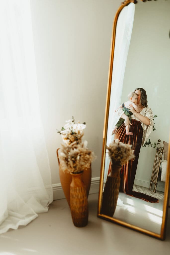 Mother holding her newborn near a mirror during a newborn session at Wildhaven Studio.