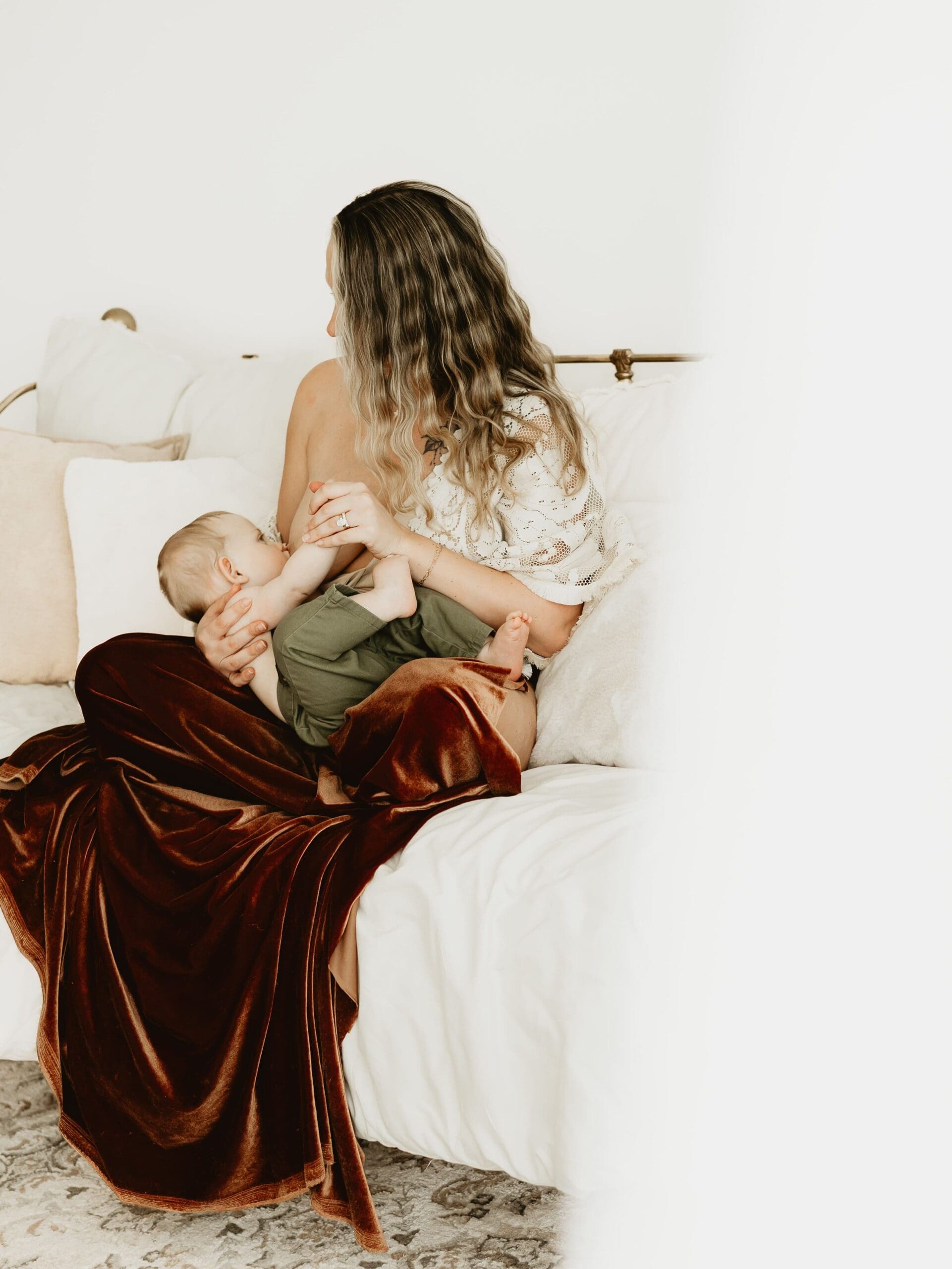 Mother nursing baby on a bed during a newborn photography session at Wildhaven Studio.