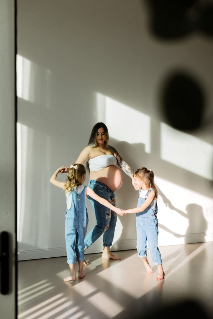 Motherhood maternity photography in Cumming Georgia capturing a pregnant mom dancing with her daughters in warm natural light at Wildhaven Studio.